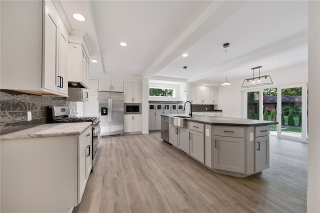 kitchen featuring light wood-type flooring, an island with sink, built in appliances, pendant lighting, and decorative backsplash