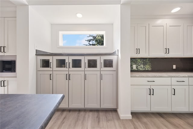 kitchen with black microwave, decorative backsplash, white cabinets, and light hardwood / wood-style floors