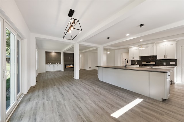 kitchen featuring white cabinets, light hardwood / wood-style flooring, decorative light fixtures, stainless steel range, and an island with sink