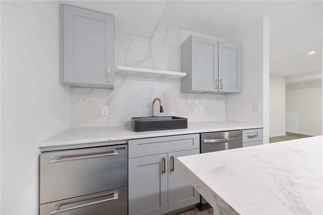 kitchen featuring tasteful backsplash, sink, light stone countertops, stainless steel dishwasher, and gray cabinetry