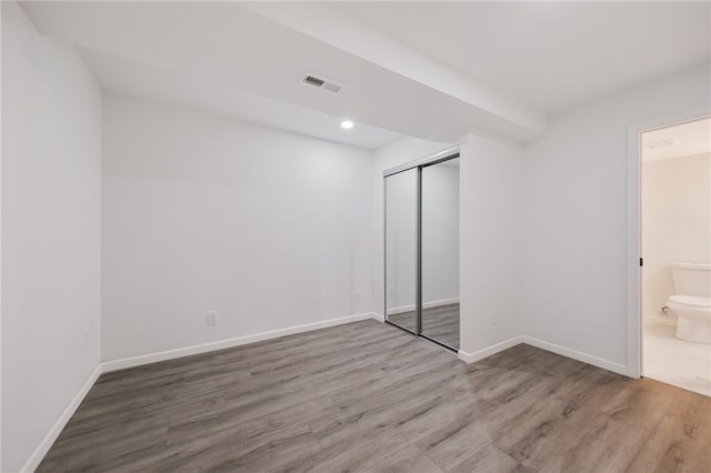 unfurnished bedroom featuring hardwood / wood-style floors, a closet, and ensuite bathroom