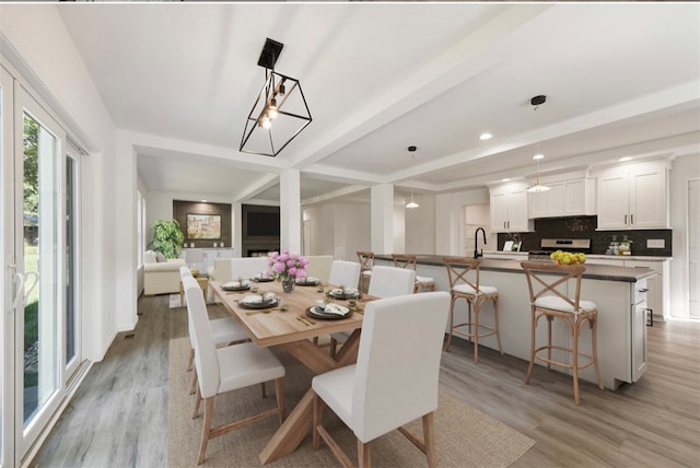 dining area featuring sink, beamed ceiling, and light hardwood / wood-style flooring