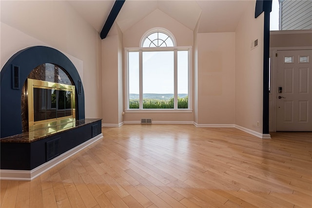 unfurnished living room featuring light wood-type flooring, high vaulted ceiling, a wealth of natural light, and a high end fireplace