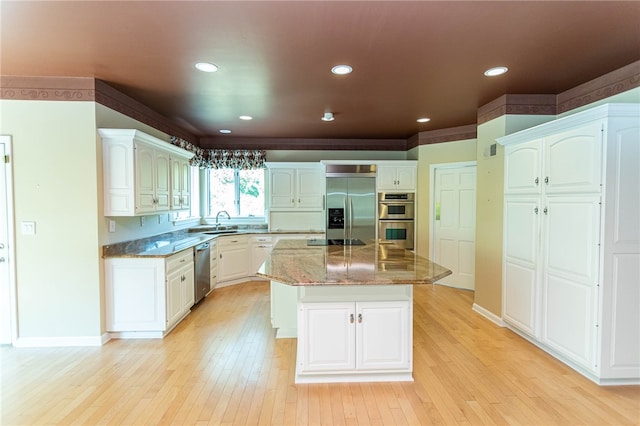 kitchen with dark stone countertops, a center island, light wood-type flooring, stainless steel appliances, and white cabinetry