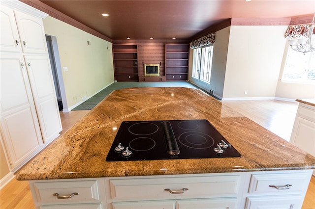 kitchen with white cabinets, a fireplace, light hardwood / wood-style floors, stone countertops, and black electric cooktop