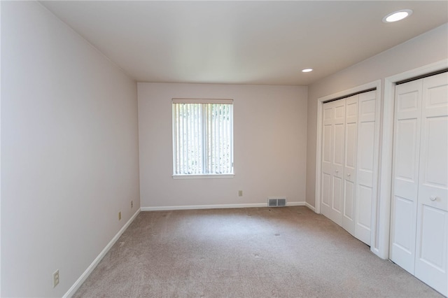 unfurnished bedroom featuring light carpet and multiple closets