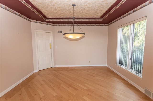 unfurnished dining area with light wood-type flooring, a tray ceiling, a chandelier, and ornamental molding