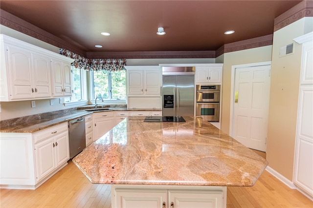 kitchen featuring stone countertops, appliances with stainless steel finishes, light hardwood / wood-style floors, a center island, and white cabinets