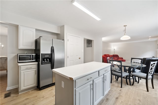 kitchen featuring light wood-type flooring, decorative light fixtures, a kitchen island, and stainless steel appliances