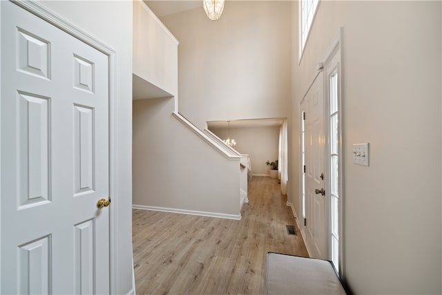 entryway with a wealth of natural light, an inviting chandelier, light hardwood / wood-style floors, and a towering ceiling