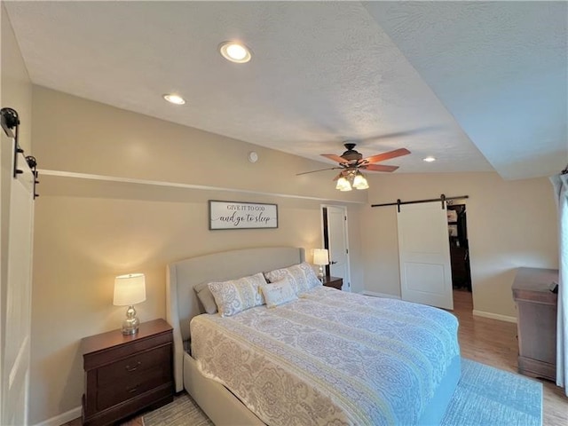 bedroom with a barn door, ceiling fan, wood-type flooring, and a textured ceiling