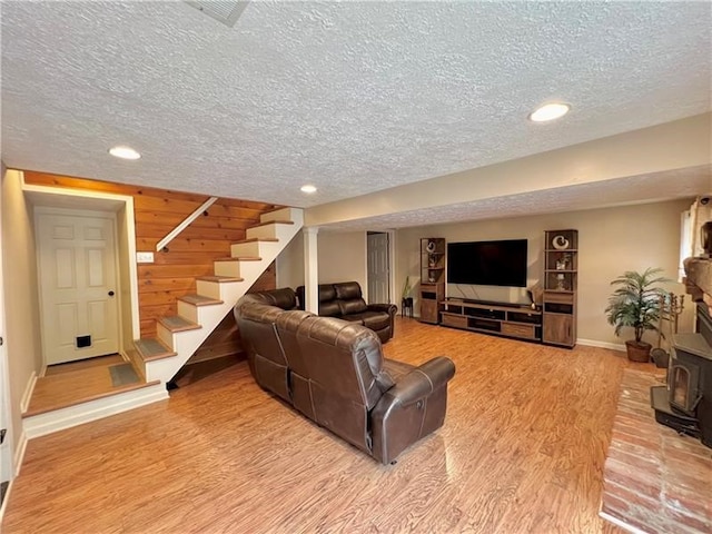 living room featuring wooden walls, wood-type flooring, a wood stove, and a textured ceiling