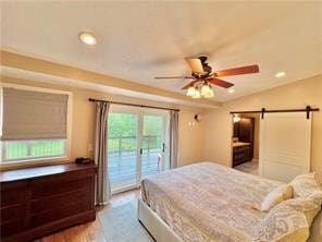 bedroom with hardwood / wood-style floors, access to exterior, ceiling fan, lofted ceiling, and a barn door