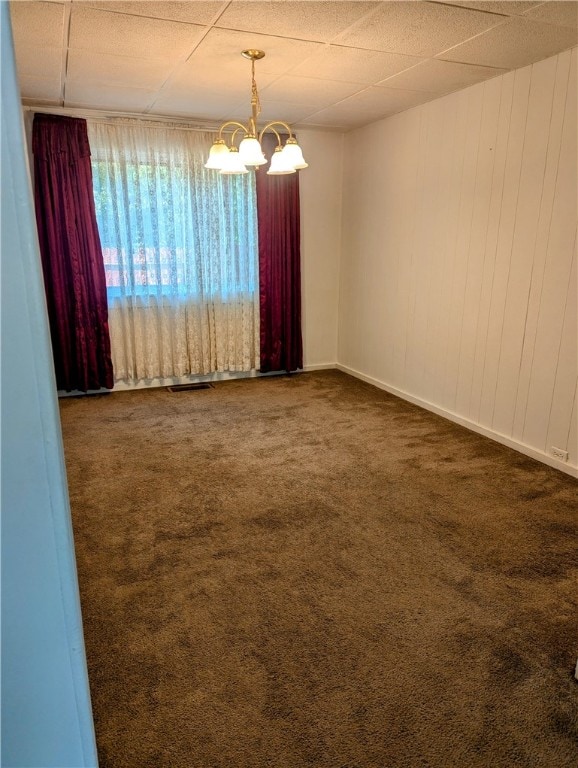 unfurnished room featuring dark carpet, a drop ceiling, and a notable chandelier