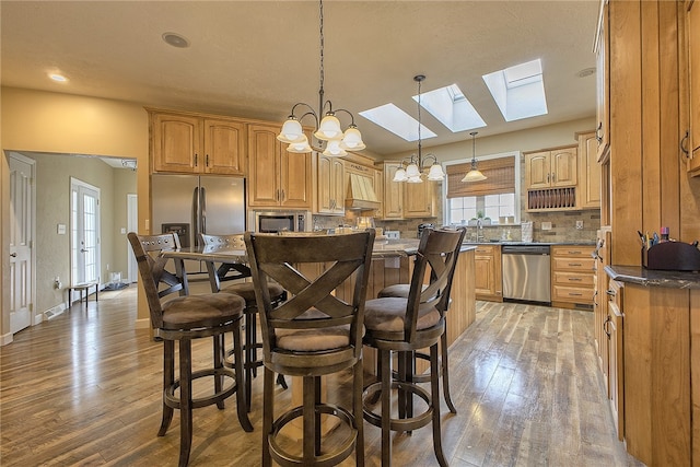 kitchen with hardwood / wood-style floors, a skylight, stainless steel appliances, hanging light fixtures, and custom range hood