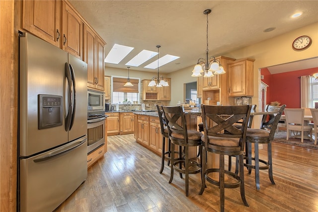 kitchen with hardwood / wood-style floors, a skylight, stainless steel appliances, decorative light fixtures, and an inviting chandelier