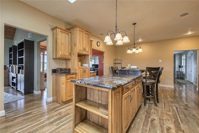 kitchen featuring hanging light fixtures, hardwood / wood-style floors, a chandelier, a kitchen island, and a breakfast bar