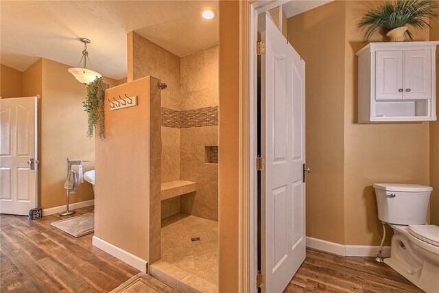 bathroom with tiled shower, toilet, and wood-type flooring