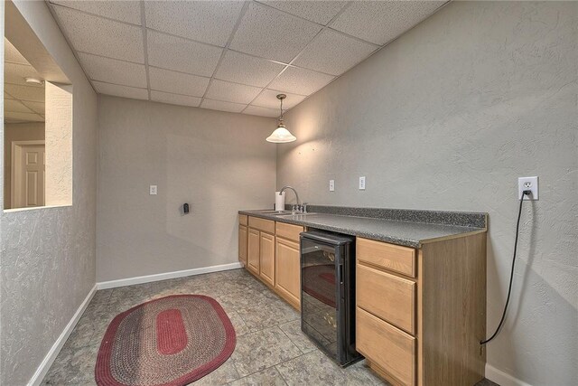 bar with a paneled ceiling, hanging light fixtures, wine cooler, and sink