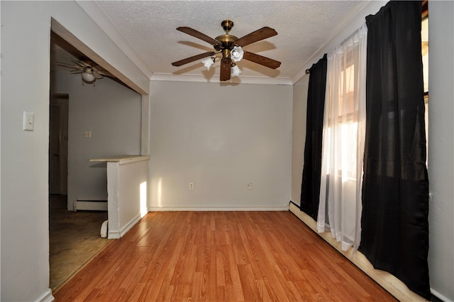 spare room with a baseboard heating unit, ceiling fan, light wood-type flooring, and a textured ceiling