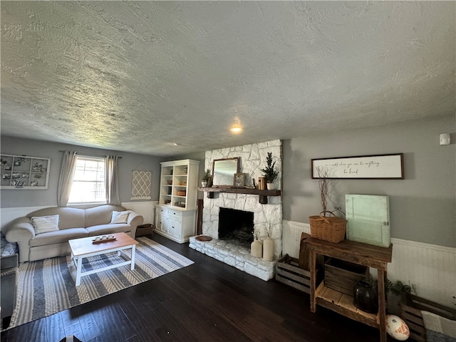 living room featuring wood-type flooring, a textured ceiling, and a stone fireplace