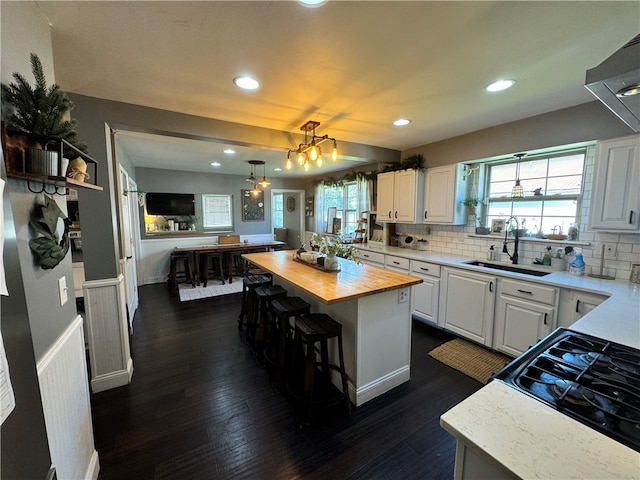 kitchen with wooden counters, white cabinetry, a kitchen island, and sink