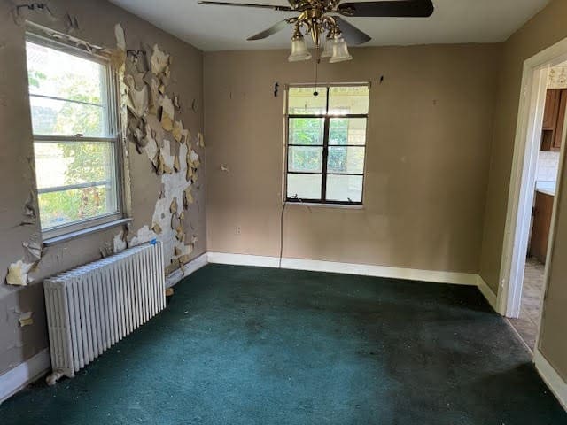 carpeted spare room with ceiling fan, radiator, and a healthy amount of sunlight