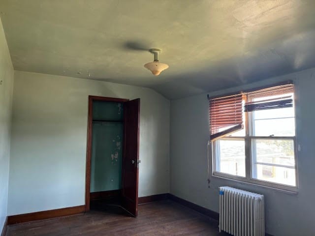 unfurnished bedroom featuring lofted ceiling, radiator heating unit, and wood-type flooring