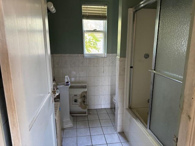 bathroom with tile patterned flooring, tile walls, toilet, and bath / shower combo with glass door