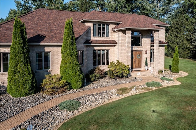 view of front of home with a front yard, brick siding, and a shingled roof