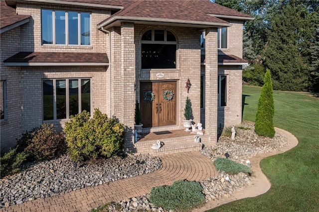 entrance to property with a yard, brick siding, and a shingled roof