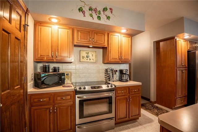 kitchen with stainless steel electric stove, refrigerator, black microwave, light countertops, and decorative backsplash