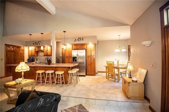 kitchen featuring baseboards, vaulted ceiling with beams, stainless steel refrigerator with ice dispenser, a kitchen breakfast bar, and brown cabinets