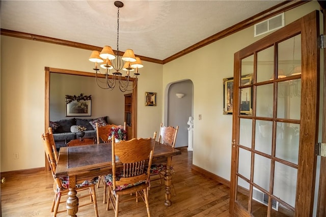 dining room with wood finished floors, visible vents, arched walkways, crown molding, and a chandelier