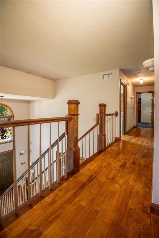 corridor with visible vents, an upstairs landing, and hardwood / wood-style floors