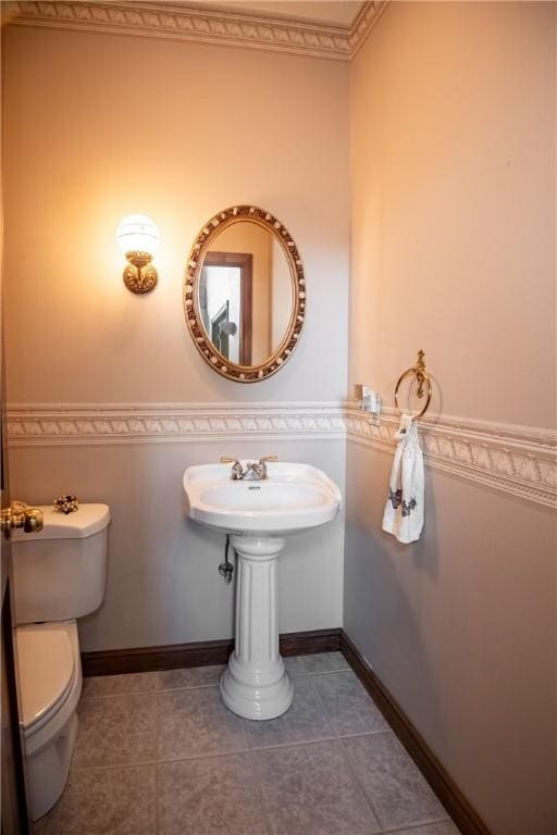 half bath featuring tile patterned flooring, toilet, and baseboards