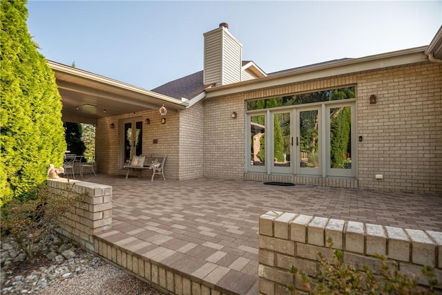 rear view of house featuring french doors, brick siding, a chimney, and a patio area