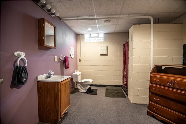 bathroom with a shower with curtain, concrete block wall, toilet, and vanity