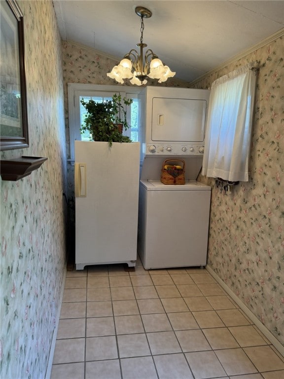 washroom with ornamental molding, light tile patterned floors, stacked washer / drying machine, and a notable chandelier