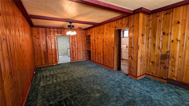 carpeted empty room featuring ceiling fan, wooden walls, and beam ceiling