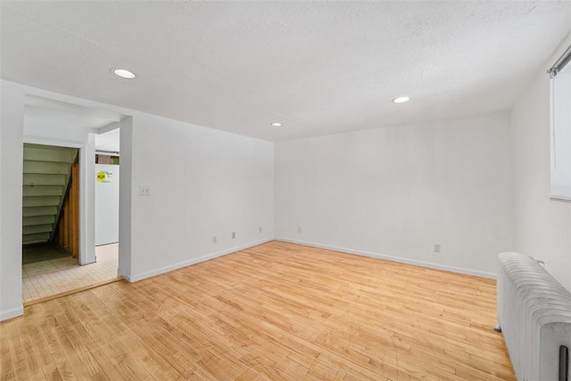 spare room with a textured ceiling, radiator, and light hardwood / wood-style flooring