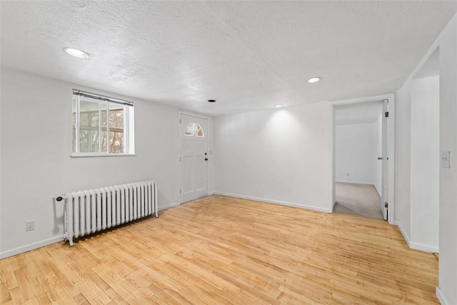 spare room featuring radiator, light hardwood / wood-style floors, and a textured ceiling