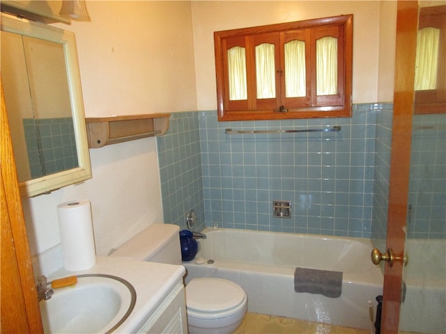 full bathroom featuring tile walls, tiled shower / bath, toilet, and vanity