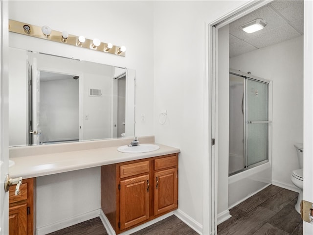 full bathroom featuring vanity, toilet, wood-type flooring, and bath / shower combo with glass door