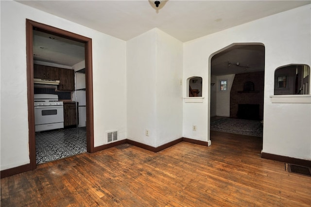 empty room with dark wood-type flooring and a brick fireplace