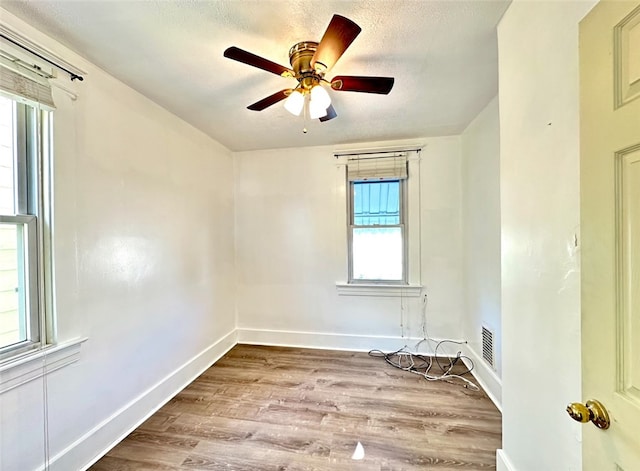 spare room with light wood-type flooring, ceiling fan, a wealth of natural light, and a textured ceiling