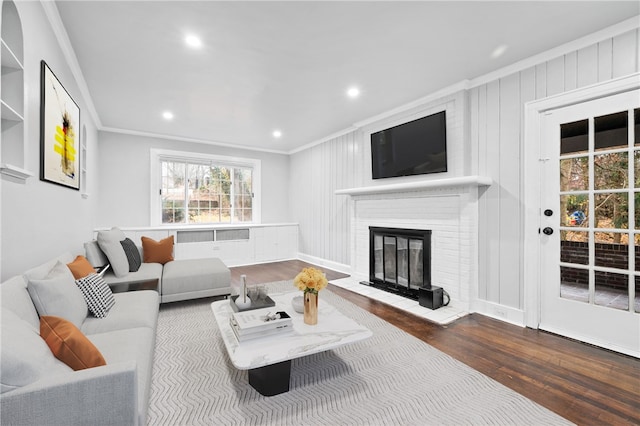 living room featuring dark wood-type flooring, ornamental molding, and a brick fireplace