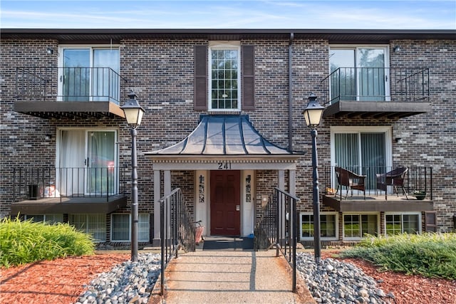 view of front of property featuring a balcony, a standing seam roof, metal roof, and brick siding