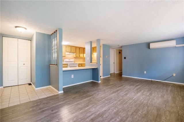 unfurnished living room featuring a wall unit AC, baseboards, and wood finished floors