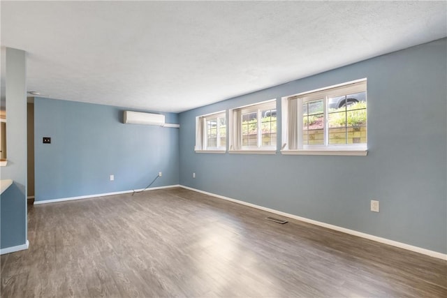 empty room featuring baseboards, a wall mounted AC, wood finished floors, and a healthy amount of sunlight